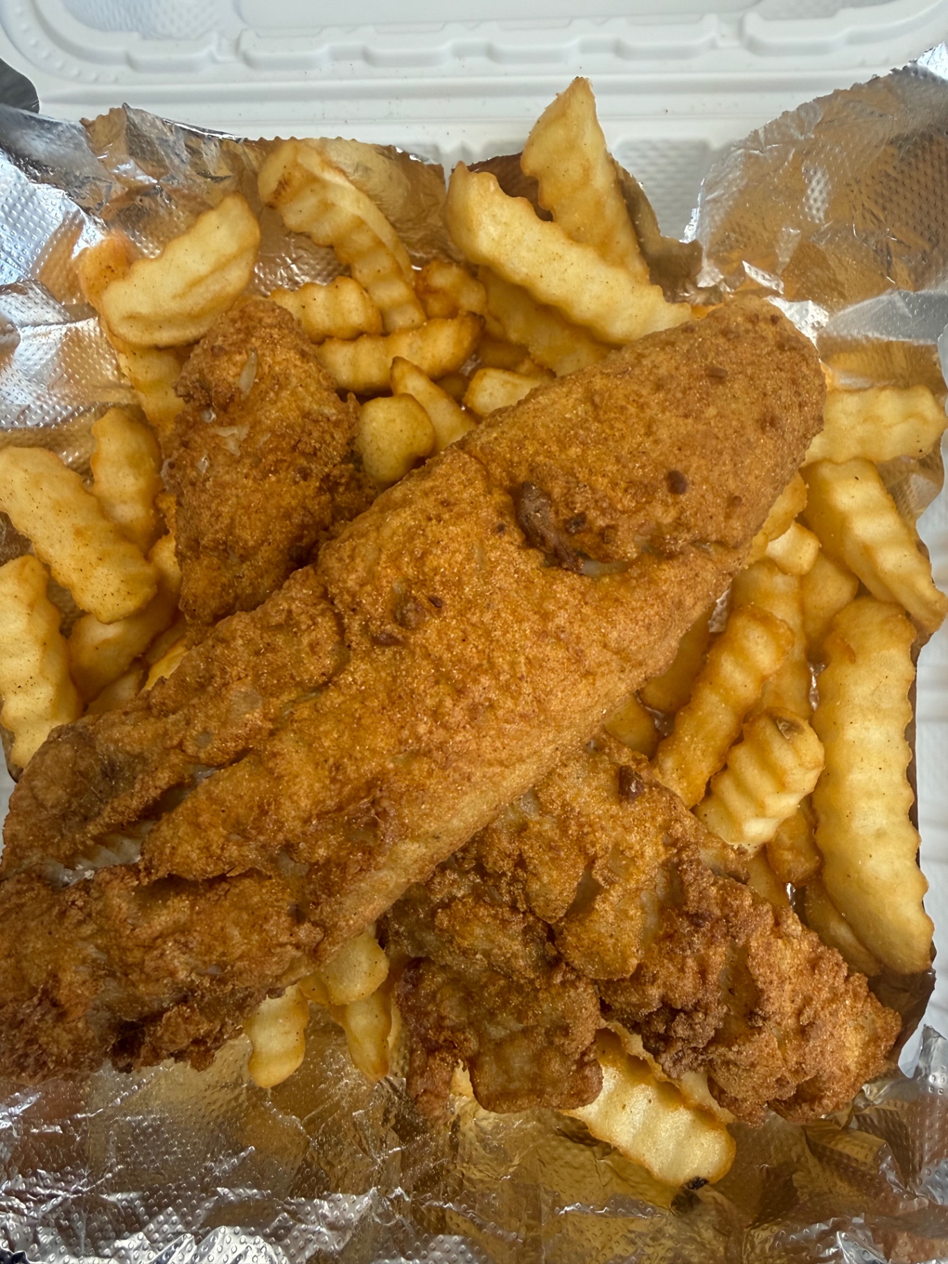 Fish dinner with seasoned fried fish fillets piled over crinkle fries
