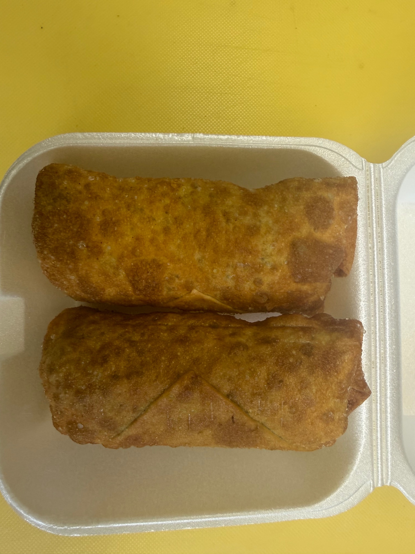 Two golden fried egg rolls in a takeout container