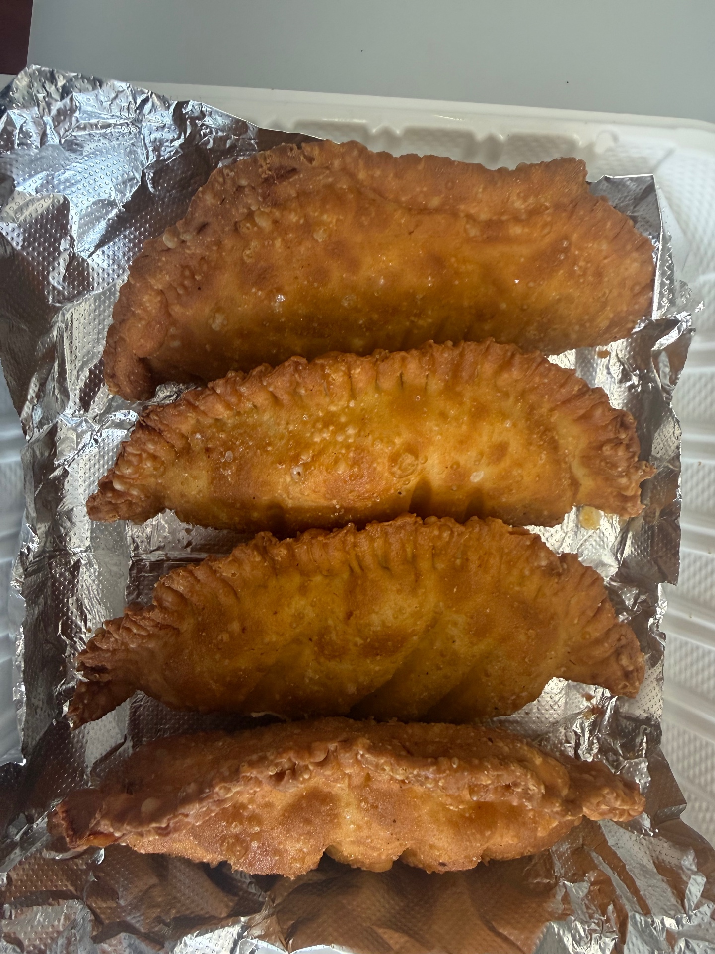 Four freshly fried empanadas lined up on foil