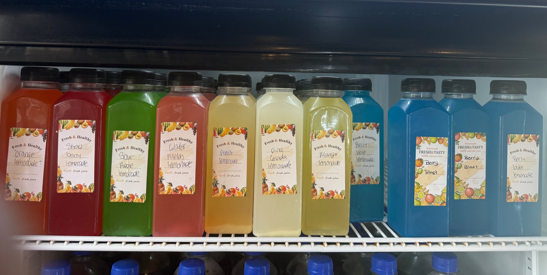 Bottles of homemade lemonade in the cooler — orange, strawberry, sour apple, watermelon, peach, pina colada, mango and berry blast